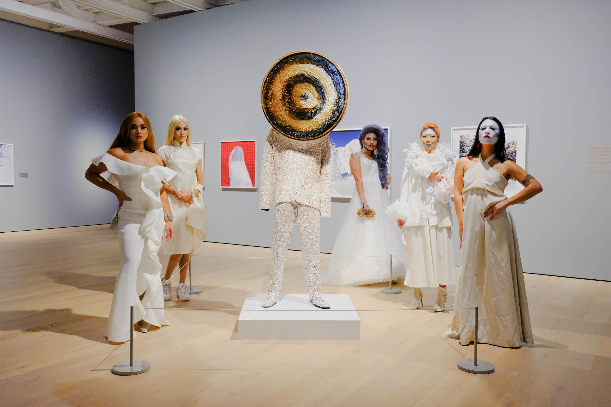 Five members of House of Rice, dressed in white, pose in a gallery around a sculptural work by Nick Cave.
